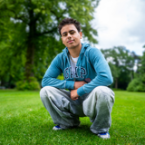 Lev is crouching on the grass in a park